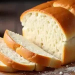 An assortment of sandwich bread loaves, including classic, whole wheat, herb and garlic, sourdough, and specialty options like cheddar jalapeño and cinnamon swirl, arranged on a rustic table